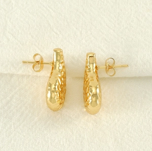 Macro shot of gold teardrop earrings with detailed hammered texture and metal backs