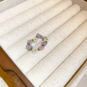 Macro view of handmade bead flower ring in purple and white on beige velvet box