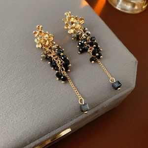 Detailed view of floral tassel earrings with black faceted beads on a velvet box
