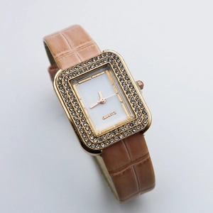 Detail of square gold watch case with double-row crystals and khaki leather strap