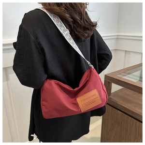 Detail of red crossbody bag featuring patterned wide shoulder strap and leather patch