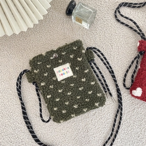 Detail of dark green plush crossbody bag with colorful textile label and rope strap