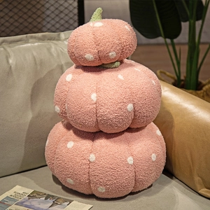 Pink polka dot pumpkin plush pillow stacked on a beige sofa in a cozy home setting