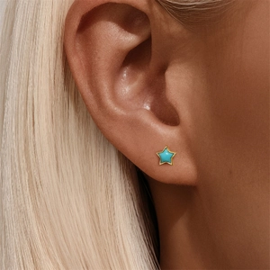 Close-up of gold star stud earring with turquoise inlay worn on an earlobe