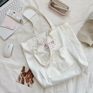 Détail du cabas en toile blanche avec broderie nœud rose et grande poche frontale