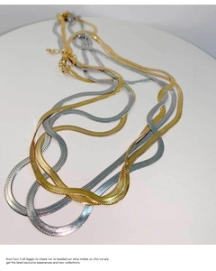 Detailed view of flat snake bone chains in gold and silver finish on a white podium