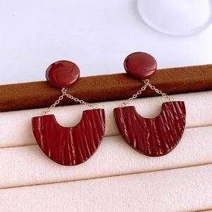 Macro view of dark red U-shaped earrings with gold chain and pleated texture details