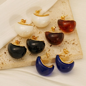 Close-up of C-shaped titanium steel earrings with resin inlays on a travertine background
