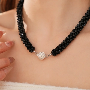 Detailed view of a black beaded necklace featuring a sparkling crystal-encrusted round charm