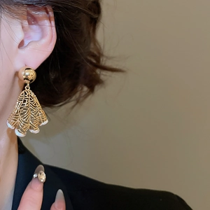 Close-up of golden fan-shaped hollow earrings with white pearls worn by a model