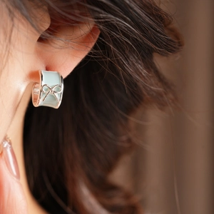 Close-up of mint green enamel C-shaped earrings with silver bow details on a model