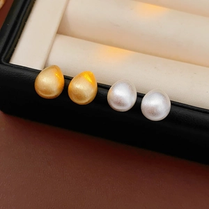 Macro detail of teardrop and round brushed metal earrings in a jewelry box