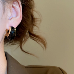 Close-up of vintage resin C-shaped hoop earrings in black and gold on a model ear