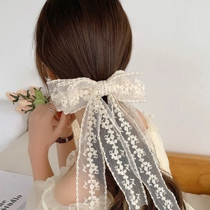 Close-up of elegant cream lace bow hair clip with long ribbons on a ponytail