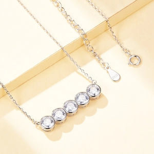 Detail showing five-stone S925 silver necklace with round cubic zirconia on yellow background