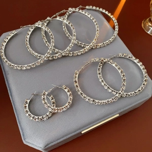 Three sizes of silver hoop earrings with shimmering crystals on a gray velvet display