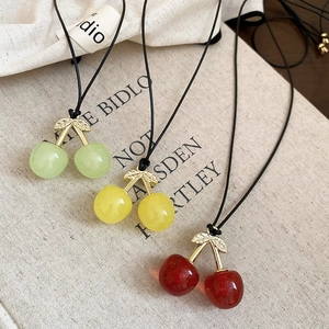 Detailed view of red, yellow, and green cherry pendants on wax cord necklaces