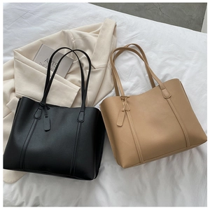 Flat lay of black and khaki large leather tote bags on white fabric with books