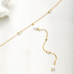 Detail showing the elegant gold-plated chain with white pearls on a minimalist background