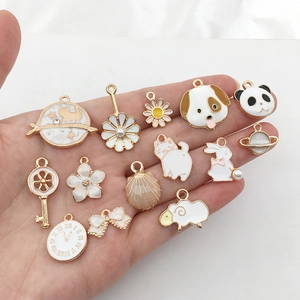 Mano che tiene vari ciondoli in smalto bianco e oro con motivi di animali e piante