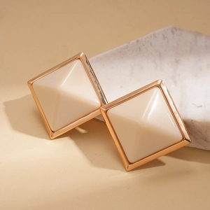 Macro view of gold geometric square stud earrings with cream resin pyramid texture