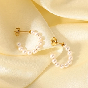Close-up of elegant gold C-shaped hoop earrings with small white pearls on satin background