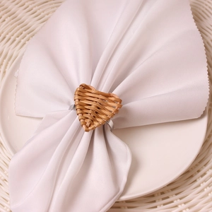 Handmade heart-shaped rattan napkin ring on white napkin with wooden dining mat