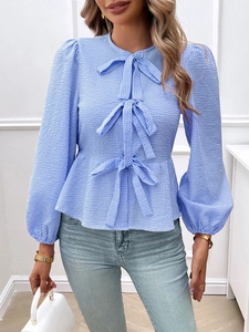 Detail view of blue plaid textured blouse with lantern sleeves and three bow tie closures
