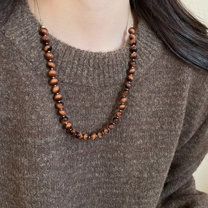 Detailed view of red tiger eye beaded necklace worn on a brown sweater background