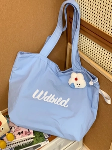 Light blue nylon tote bag detail with white bunny charm and wide shoulder strap