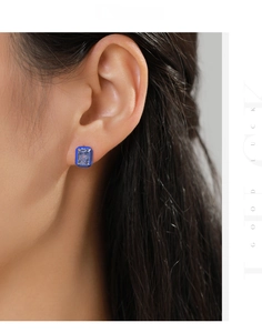 Macro shot of rectangular blue zircon earrings with dark blue enamel border on model ear