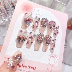 Macro detail of nude pink press-on nails with luxury heart crystals and silver bow charms