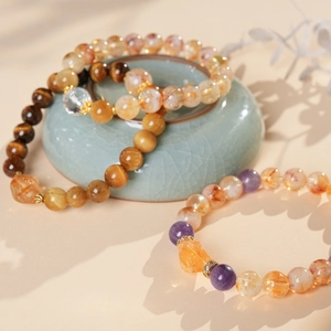 Close-up of beaded bracelets with amethyst, tiger eye, and citrine next to a ceramic bowl
