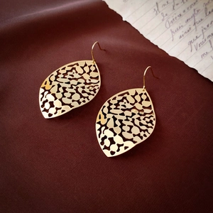 Macro shot of gold hollow leaf tassel earrings with vintage abstract metal textures