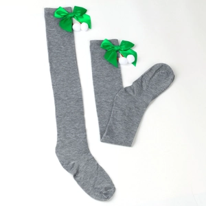 Close-up of grey knit over-knee socks with green satin bows and white faux fur pom-poms