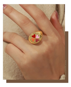Détail d'une bague chevalière dorée avec un motif trèfle à quatre cœurs colorés au doigt