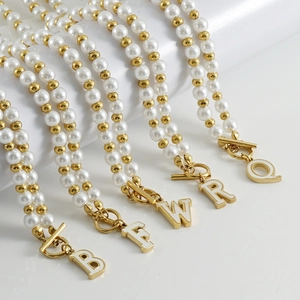 Vue détaillée de colliers de perles dorés 18K avec fermoir OT et pendentifs lettres