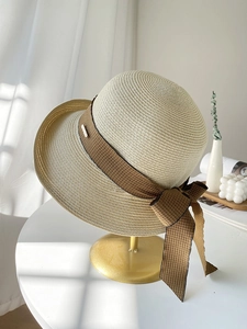 Détail d'un chapeau de paille avec ruban marron et petit logo en métal décoratif