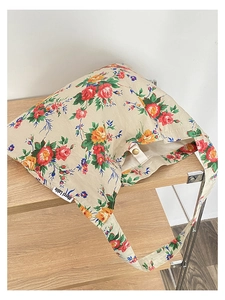 Detail of floral canvas tote bag with red and yellow roses on a vintage wooden stand