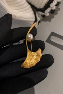 Dettaglio macro di una spilla a foglia di ginkgo dorata con perla su velluto scuro
