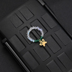Macro detail of elastic bead ring with green crystals and a gold butterfly charm