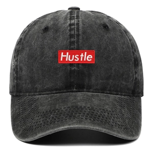 Detailed view of white Hustle embroidery on a red patch on washed black denim baseball cap