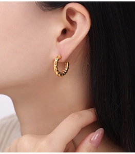 Close-up of elegant golden C-shaped hoop earrings with spiral texture on a female model