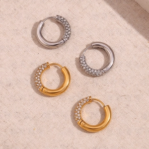 Dettaglio di orecchini a cerchio in oro e argento con zirconi incastonati su lino
