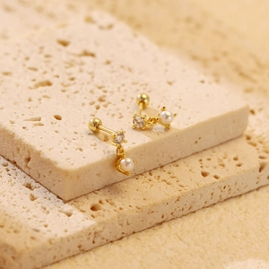 Macro shot of gold pearl stud earrings with zircon stones on a textured stone surface