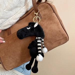 Black flocked horse keychain with striped scarf hanging on a brown suede handbag