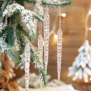 Set of clear acrylic icicle ornaments hanging on a snowy Christmas tree with warm lights