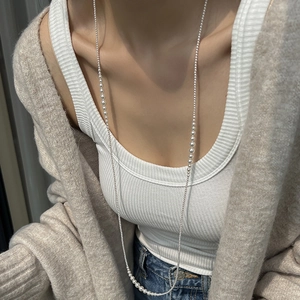 Elegant long pearl necklace draped on a white vest for a minimalist luxury fashion look