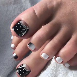 Detail of black and white press-on toenails with polka dots and bowknot design