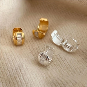 Close-up of gold and silver square zircon hoop earrings on a beige knit background